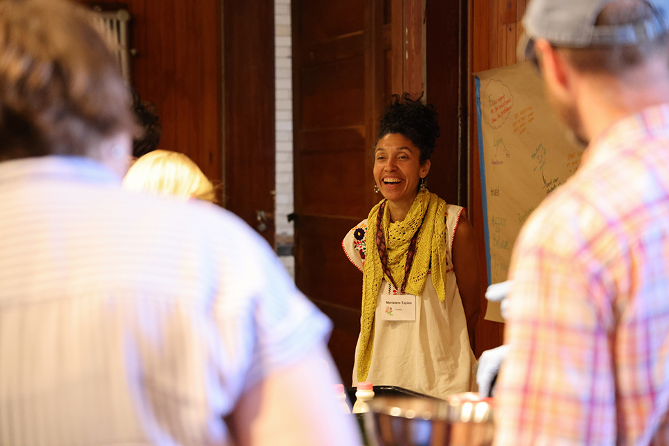 A woman smiles during a cooking demonstration with peoples' backs to camera in foreground