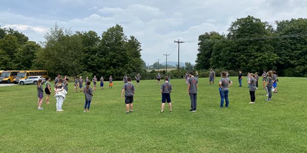 Students stand in large circle on grassy field