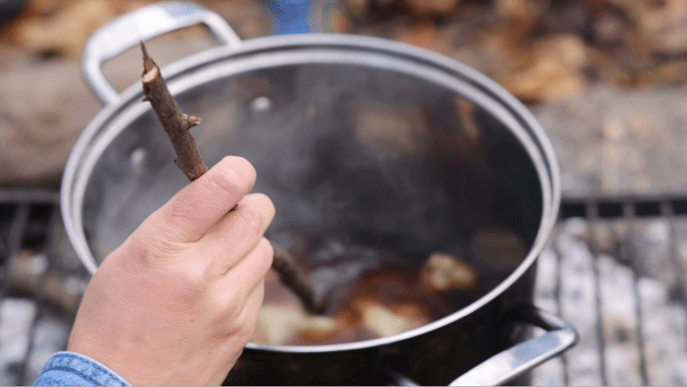Dark clothing dye is stirred in a pot over a fire