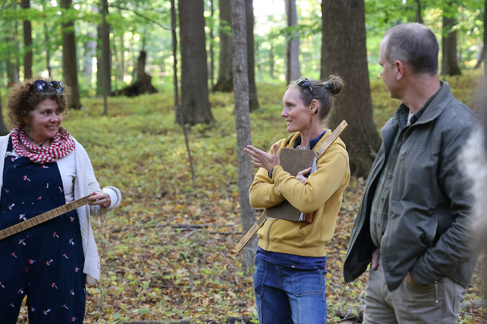 three people in a forest talking. One woman holding a Biltmore stick
