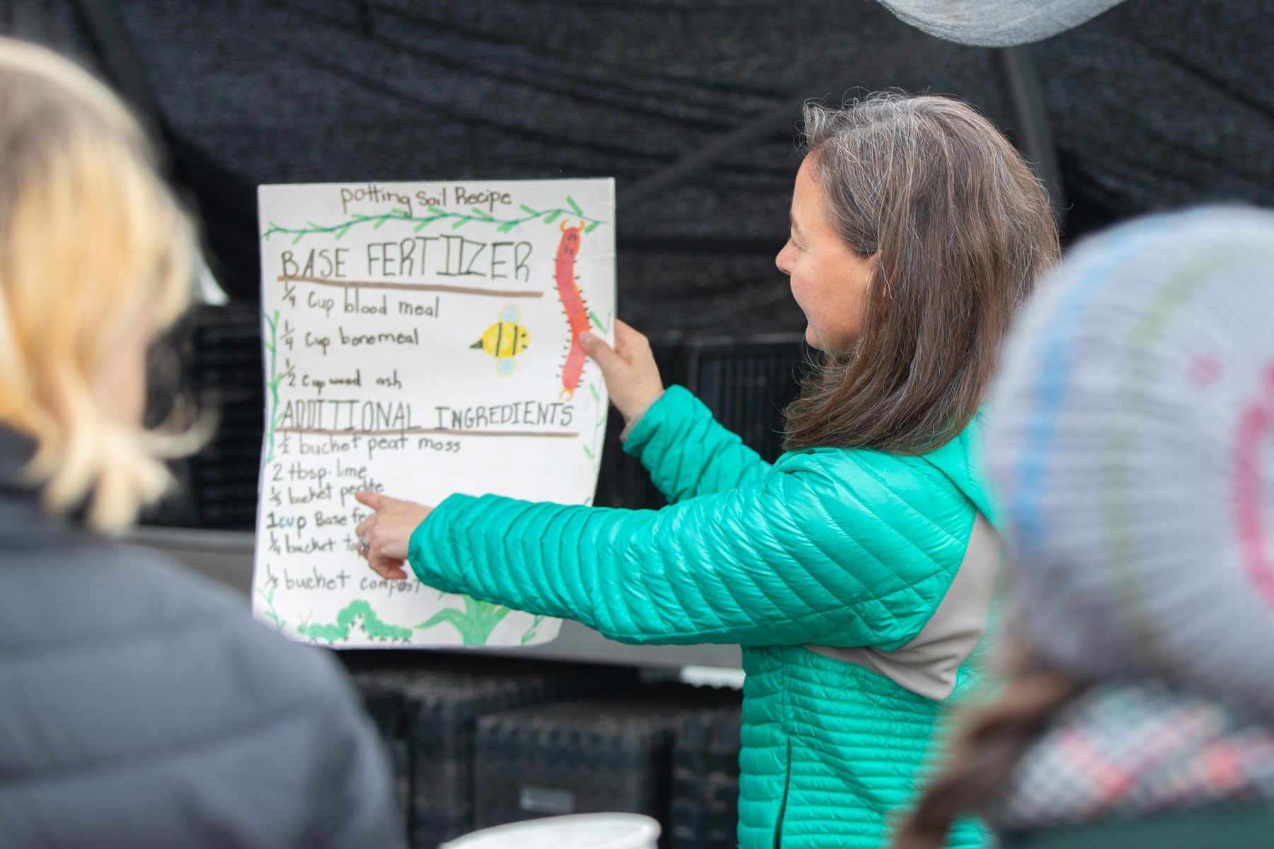 A person is holding and pointing to a poster titled "Potting Soil Recipe" with sections for "Base Fertilizer" and "Additional Ingredients." 
