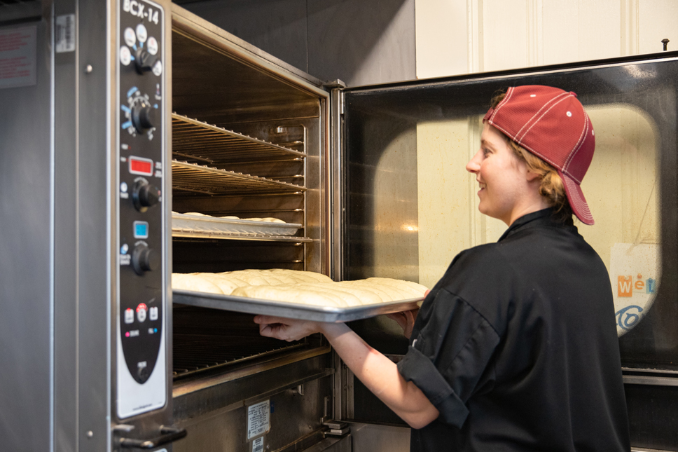 A woman pulls a tray of freshly baked rolls out of an oven