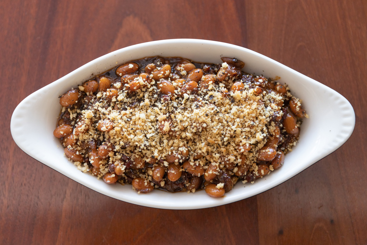 A dish filled with Maple Black Pepper Baked Beans, topped with breadcrumbs.