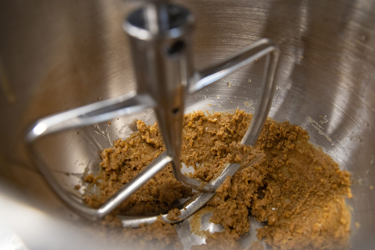 A close-up view of tahnini being mixed in a metal stand mixer with a paddle attachment.