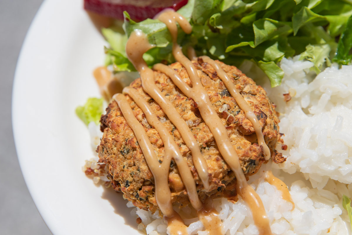 A plate of food featuring a falafel patty drizzled with a sesame dressing sauce, served on a bed of white rice a fresh green salad.