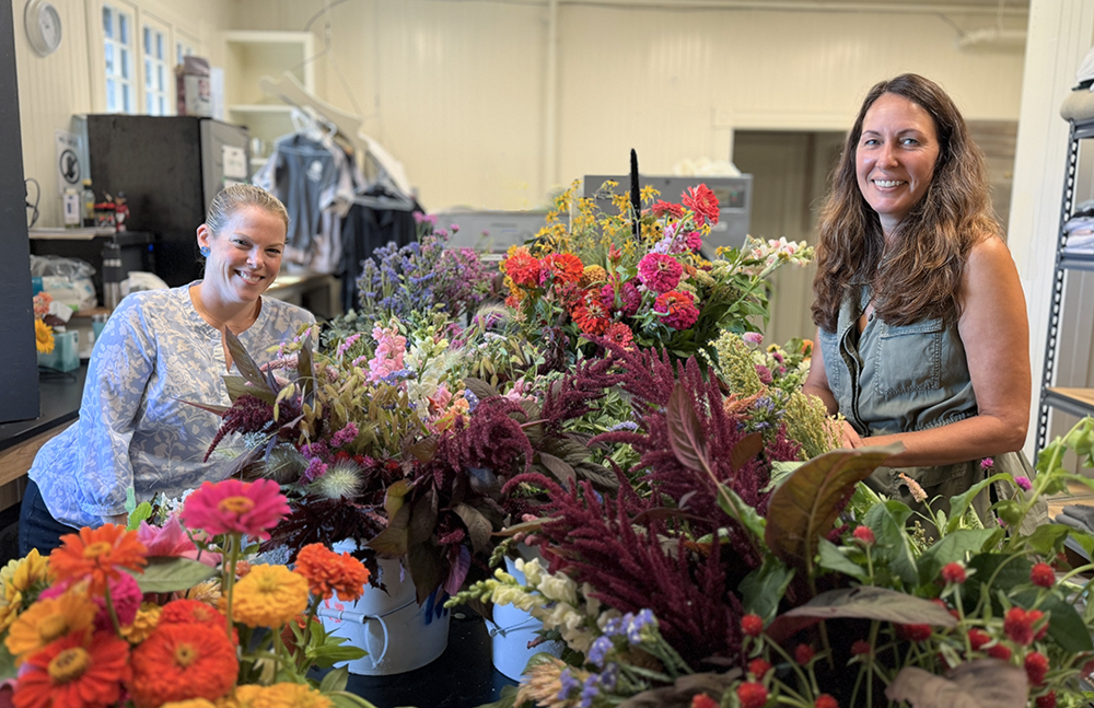 two women on either side of a table full of cut flowers.