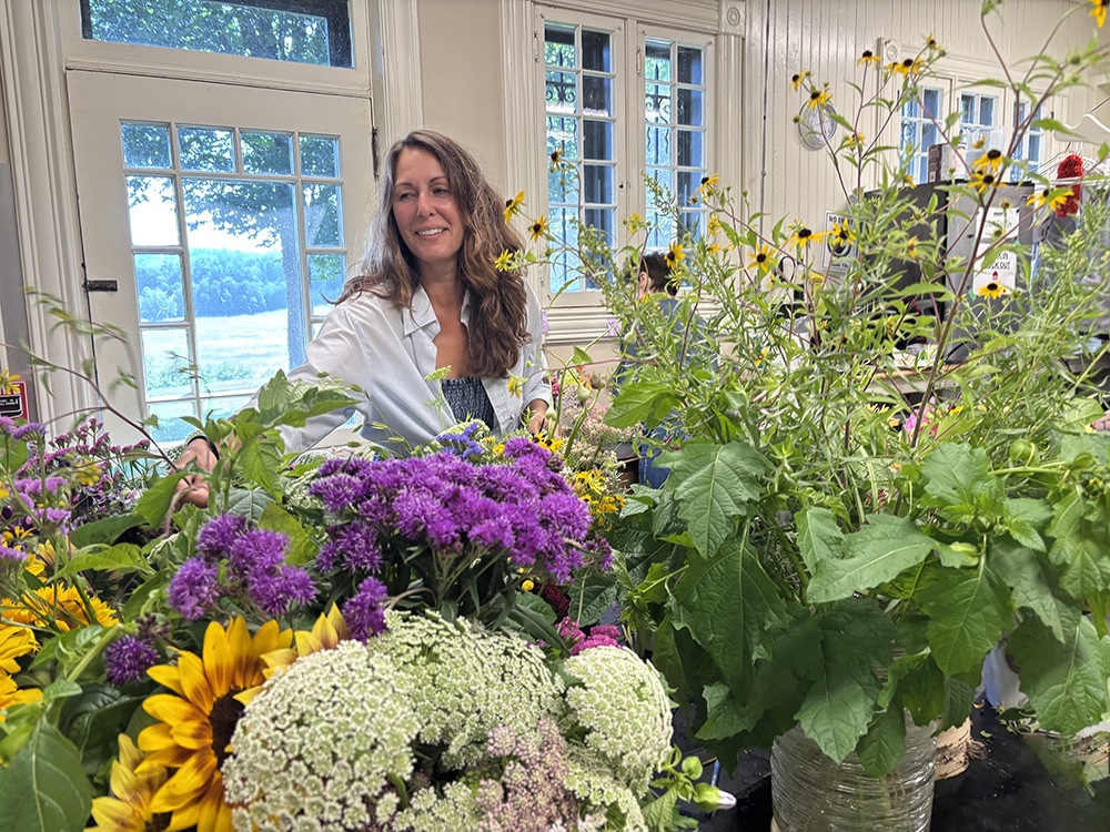 woman with long brown hair stands behind a table full of cut flowers