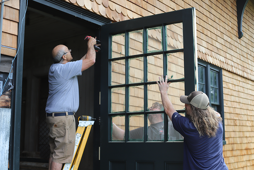 3 men attaching door to its hinges on outside of breeding barn