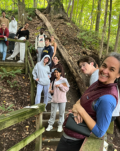 An adult and a dozen high school students smile while standing on wooden stairs on a forested trail