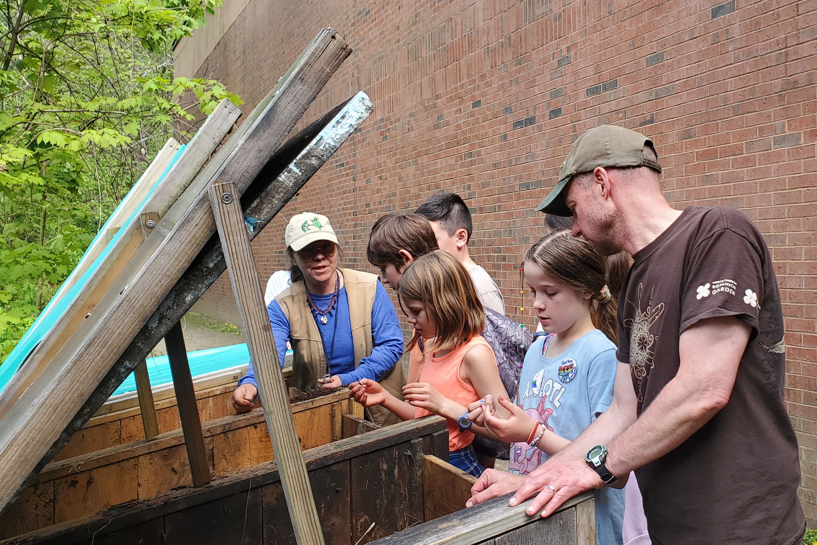 Young people and adults inspect large outdoor compost buckets