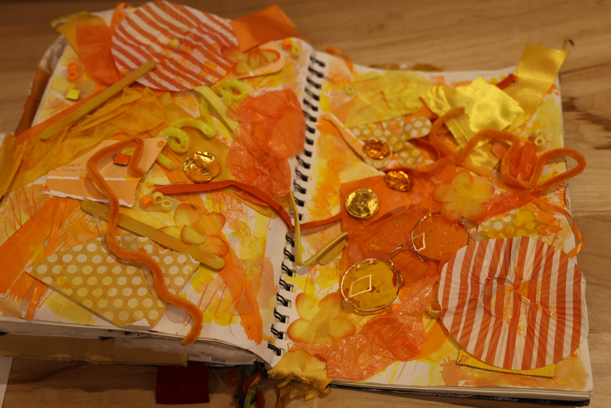 A journal sits on a table open to a spread with collaged orange materials