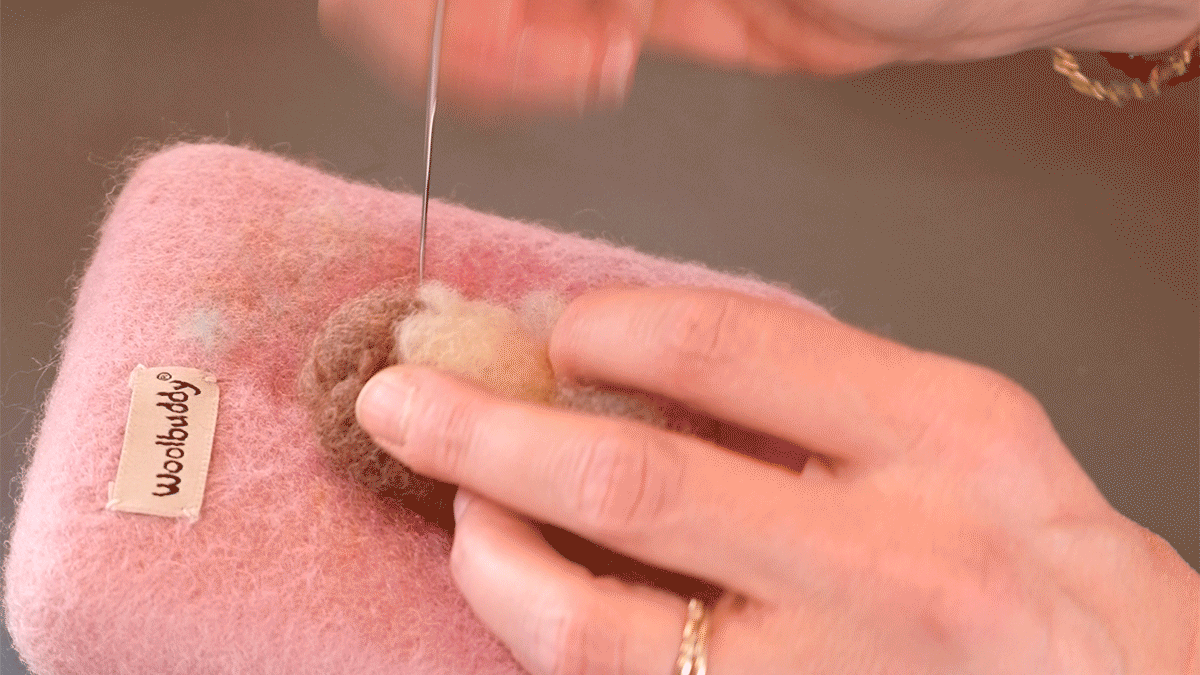 A person works a small ball of brown wool with a needle
