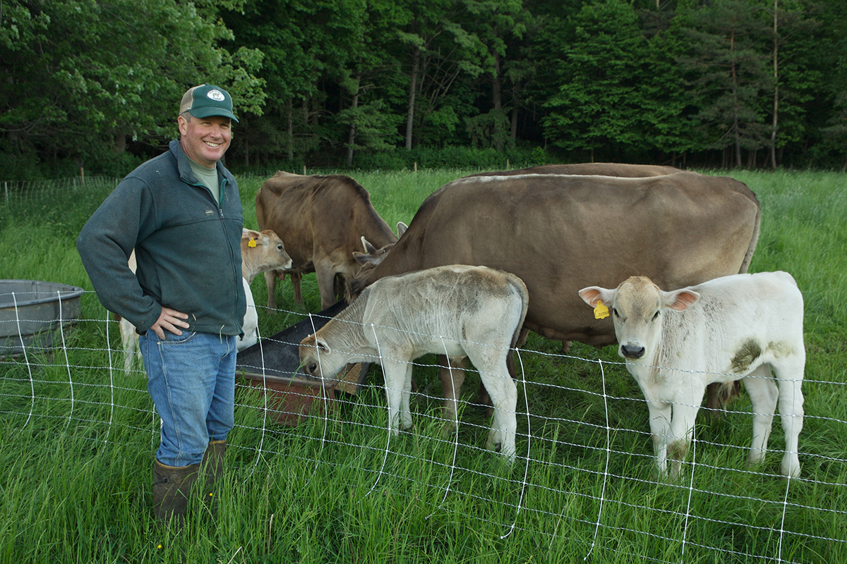 Sam dixon stands in baseball hat and jeans beside cows and calves in a pasture
