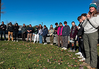 A group of high school and college aged students stand in a circle on grass