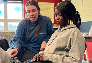Two young people work together on a laptop in a classroom