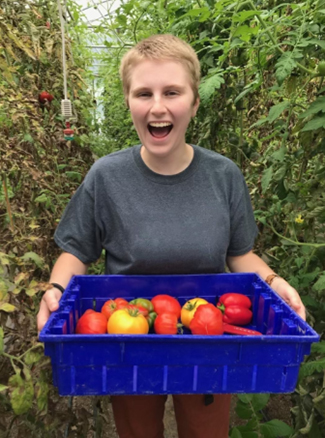 A woman smiles broadly holding a flat of tomatoes in a greenhouse