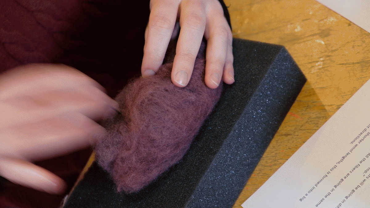 A closeup of a person's hands poking purple wool with a needle