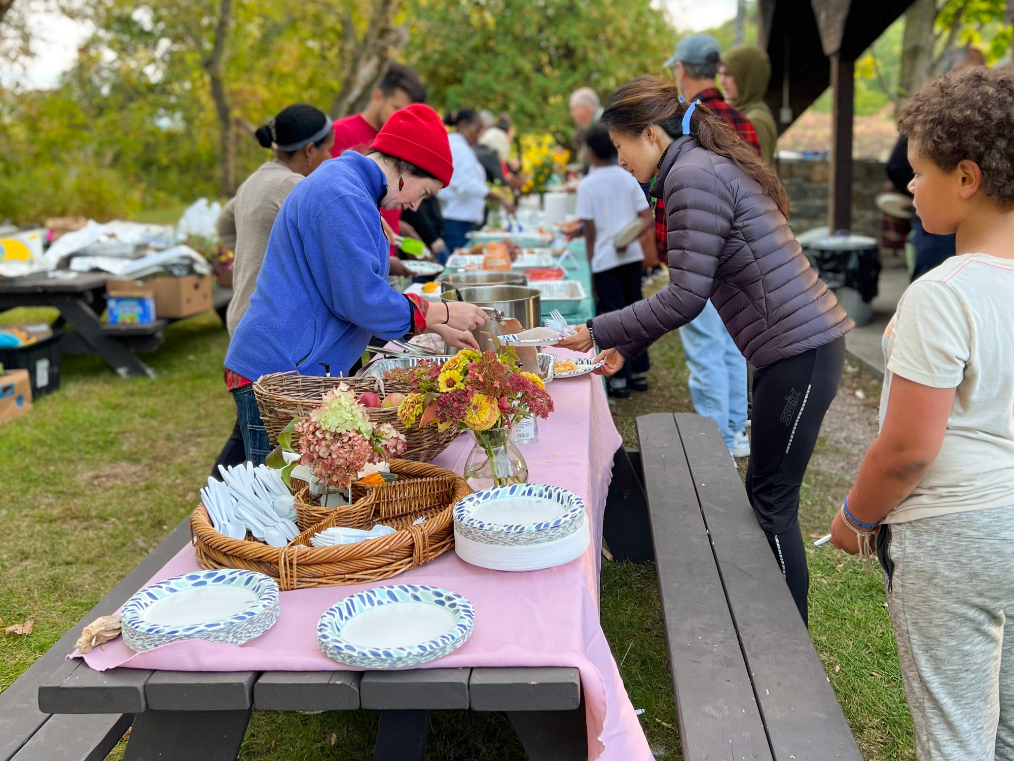 People line up at picnic tables, full of food to share