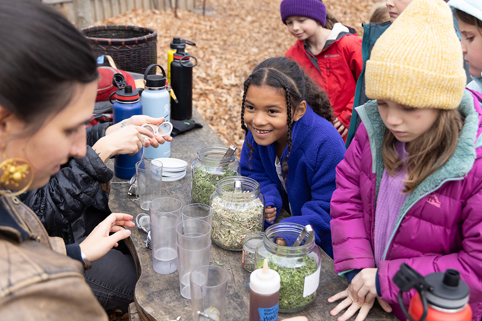 A group of young children make tea at an outdoor table