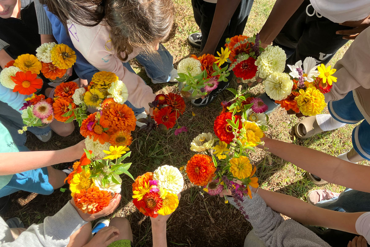 A group of students standing in a circle, each holding a bouquet of colorful flowers including orange, yellow, and white blossoms.