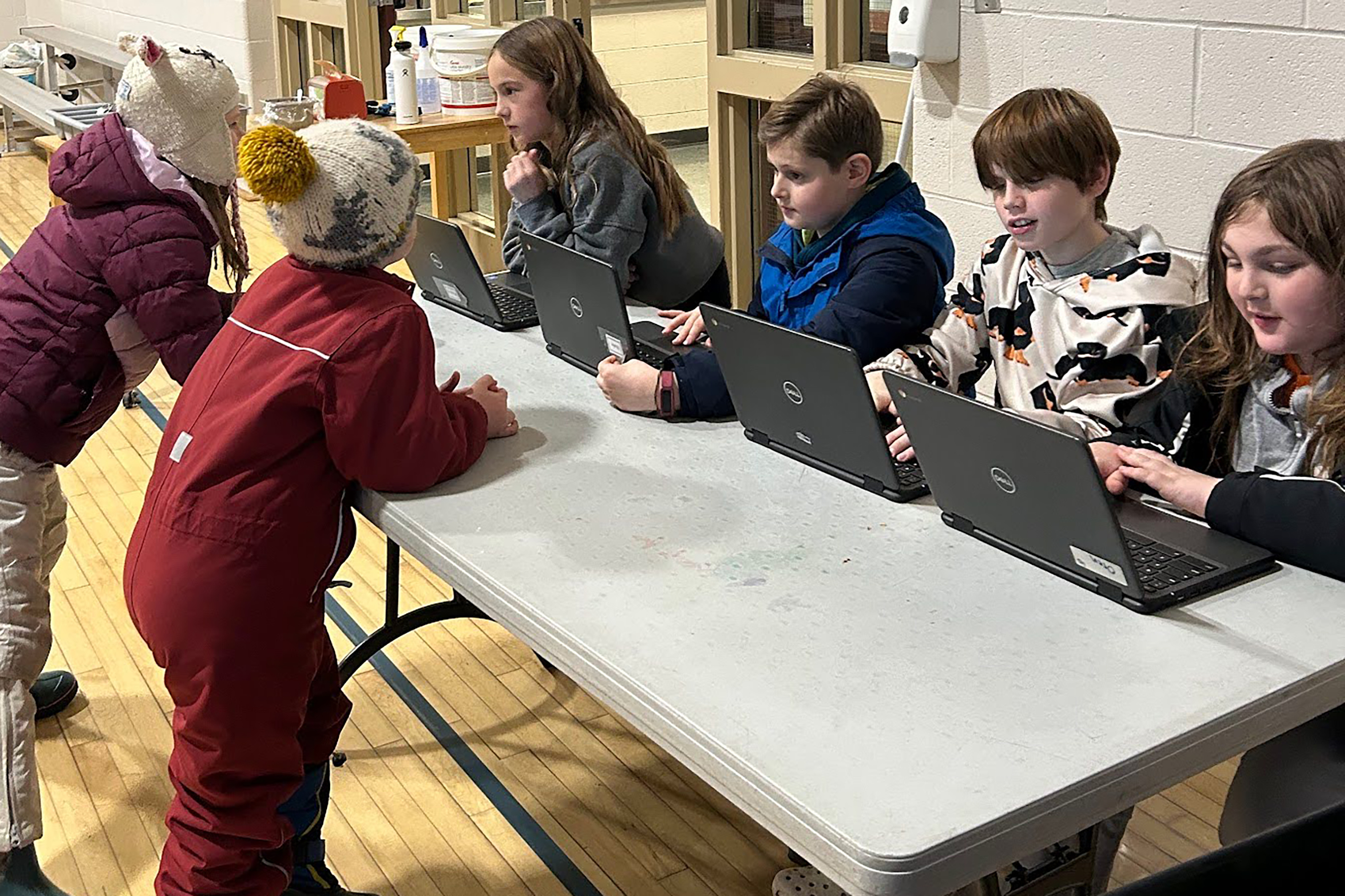 Four young students sit behind laptops conducting interviews in a school cafeteria