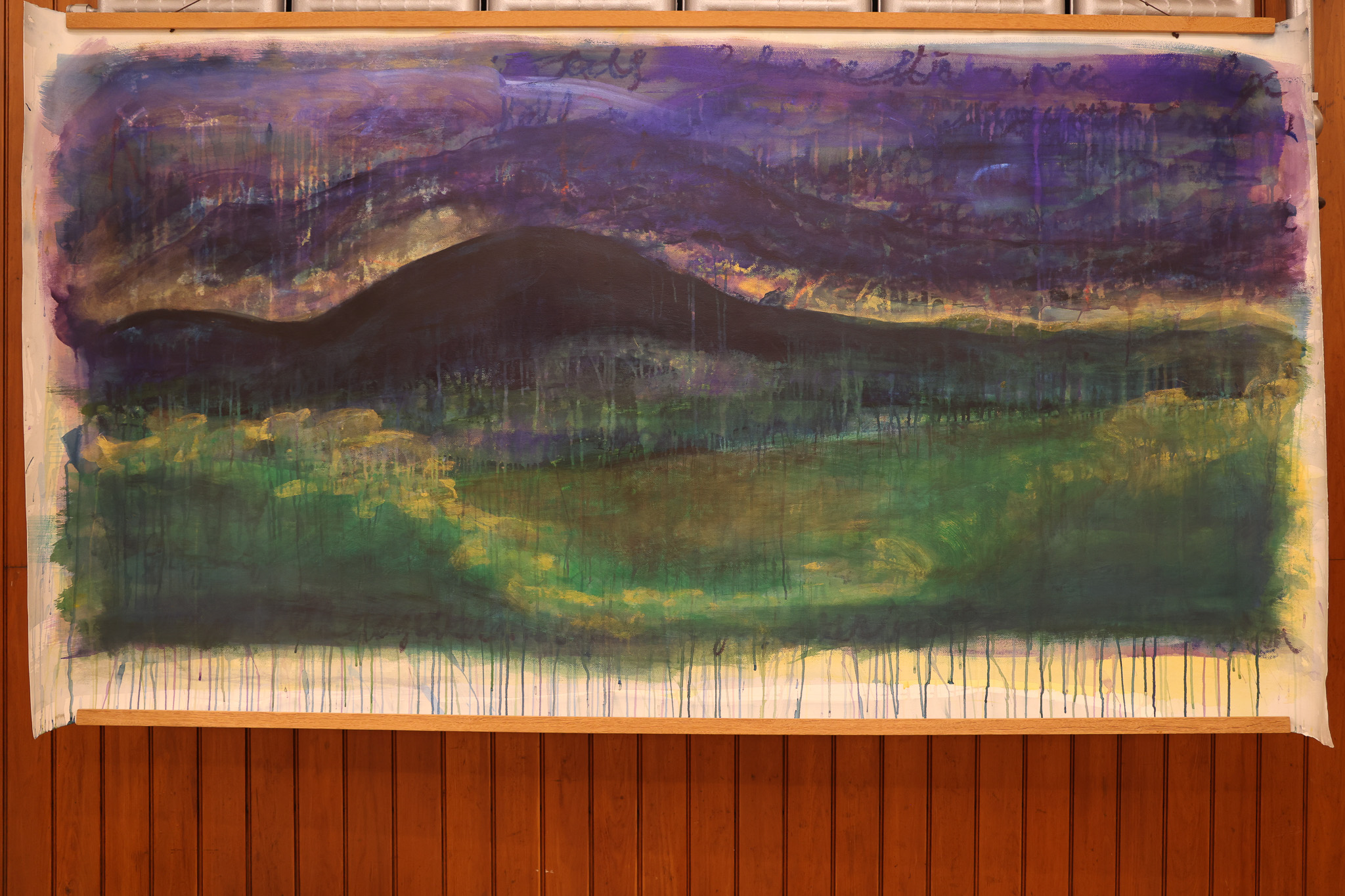 A large painting depicting green mountains against a purple background