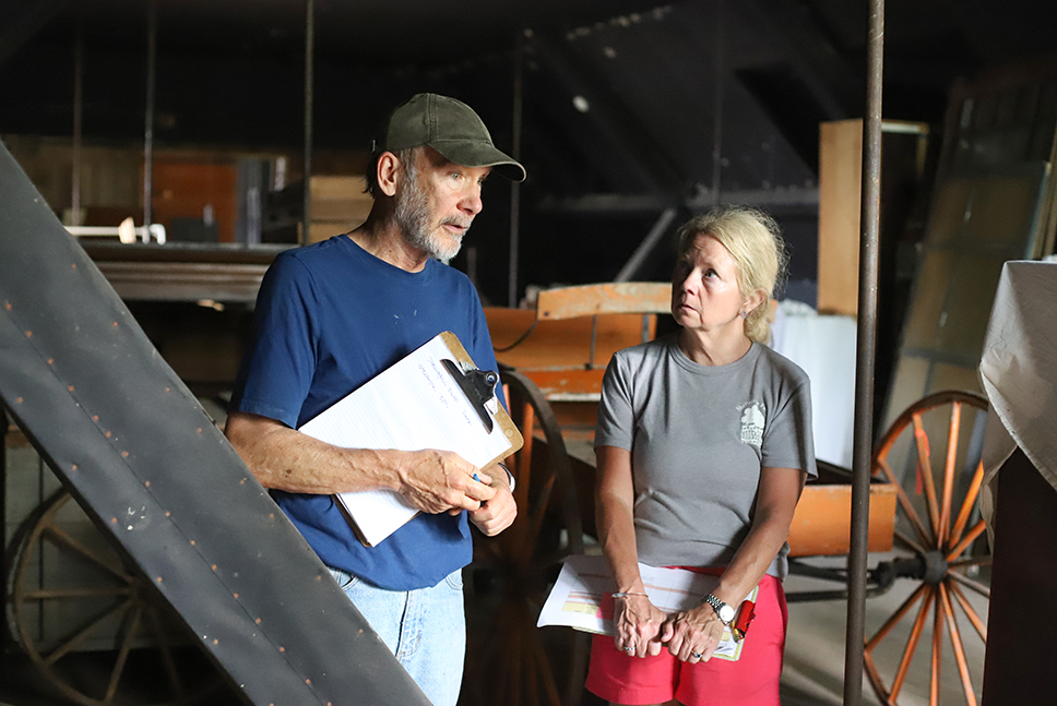 Man and woman with clipboards surveying items in attic of Coach Barn