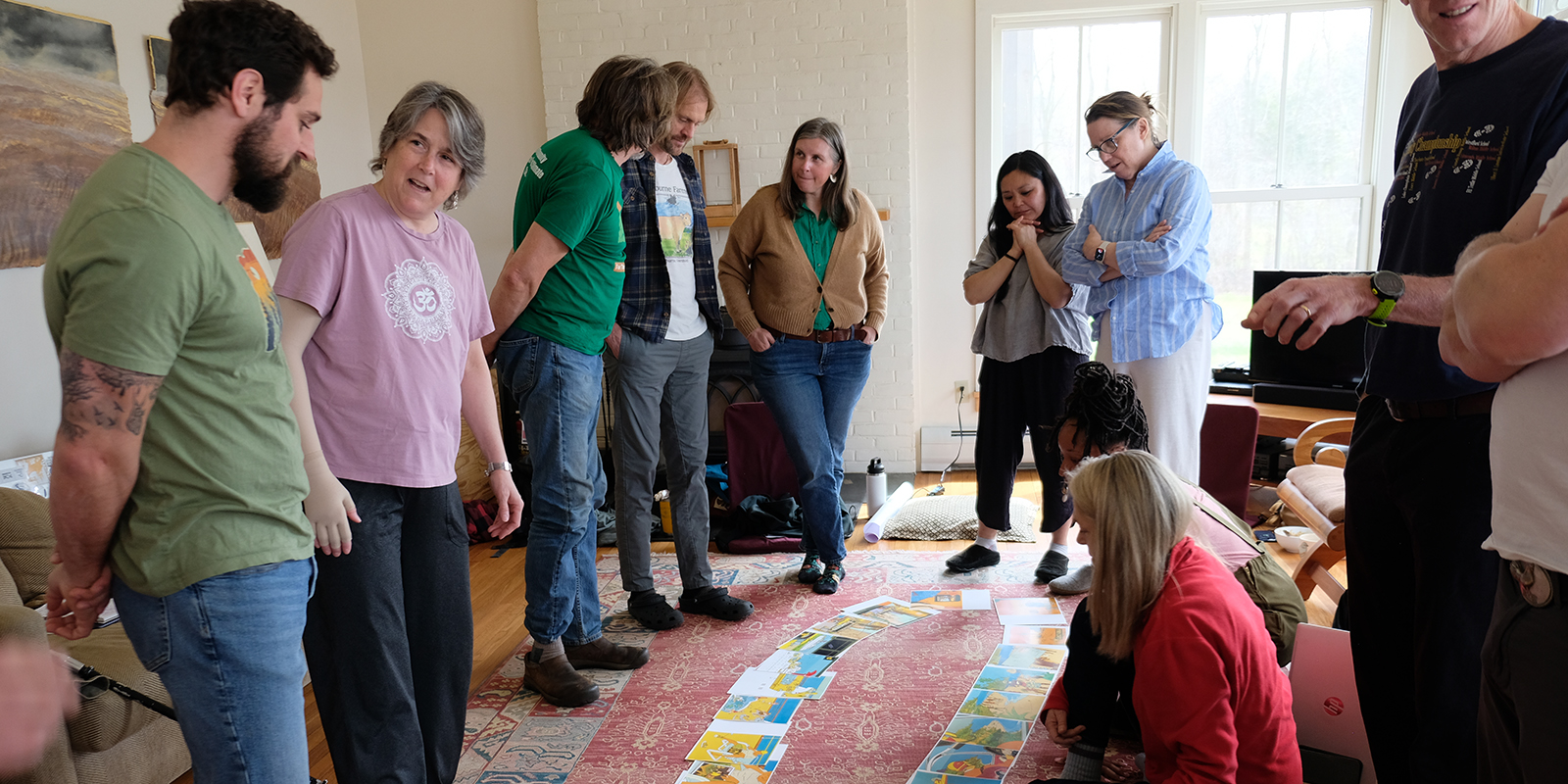 A group of adults in discussion in a living room gathered around pages of a picture book spread on the floor