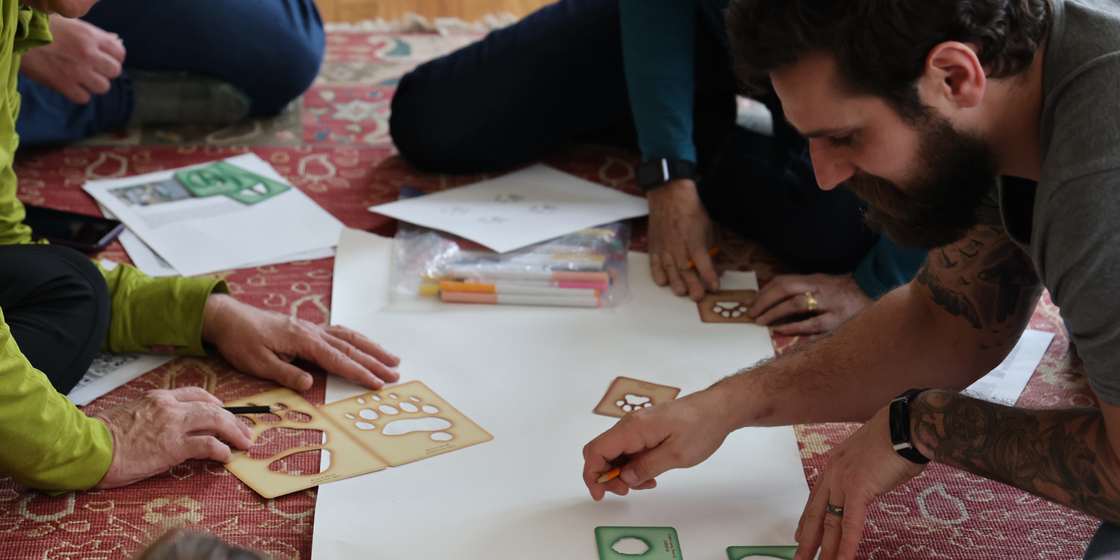 Several adults trace animal track stencils on a large piece of white paper