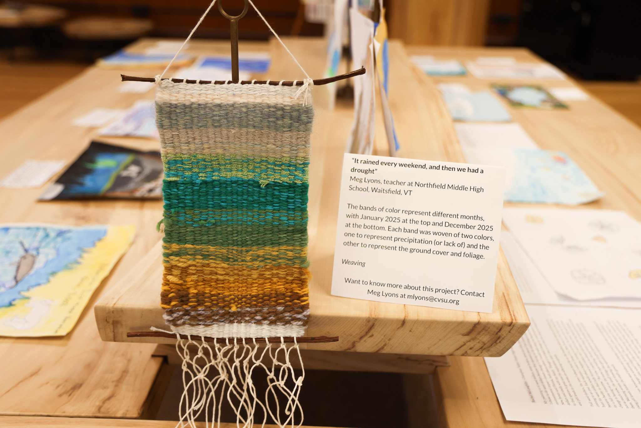A small weaving of earth toned fibers sits on a table