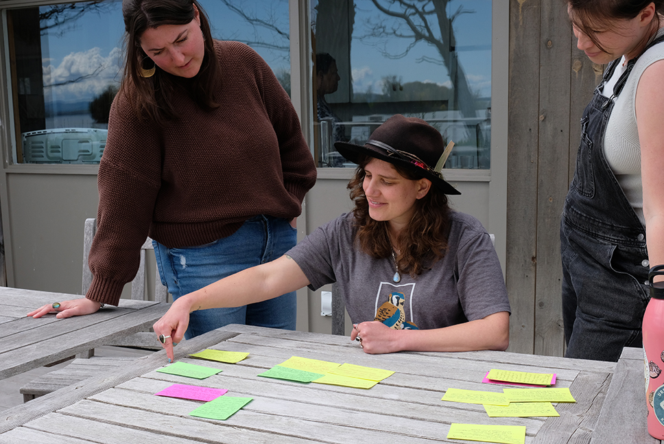 Three people gather around an outdoor table looking at colorful index cards
