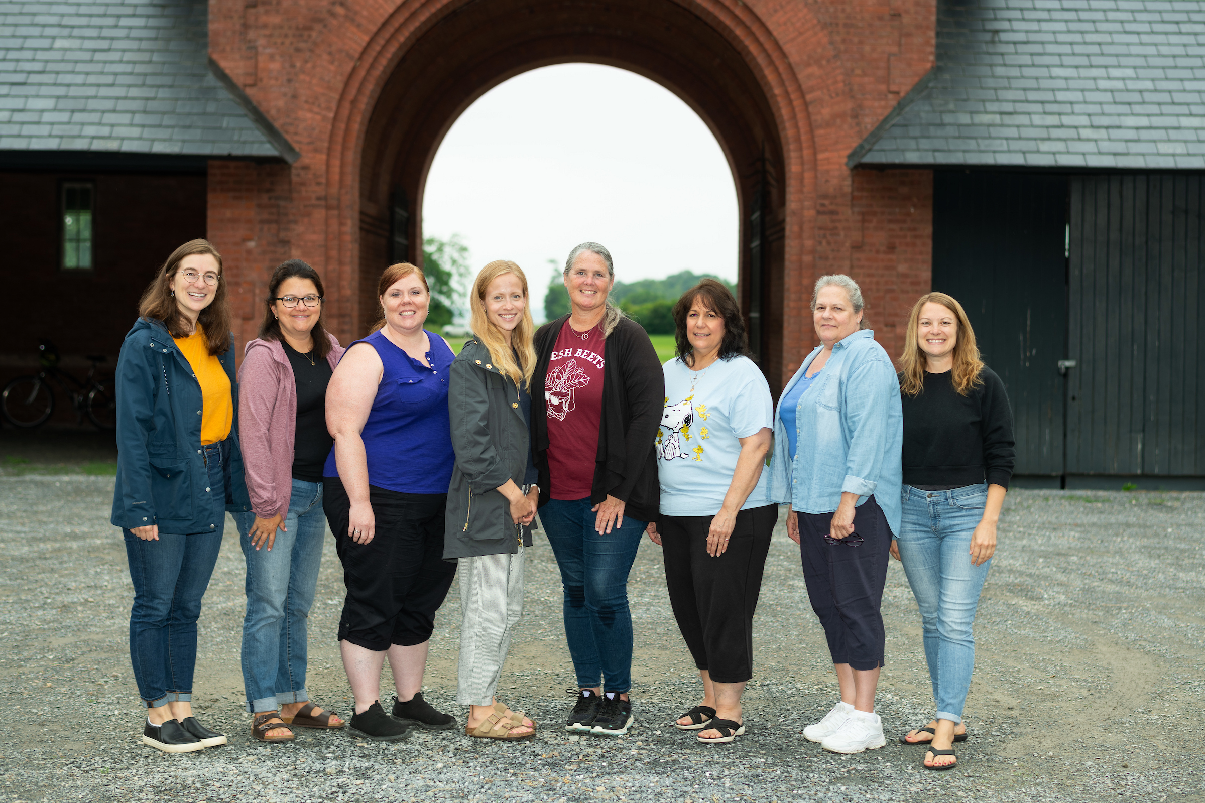 Group of eight people standing and smiling in front of a large brick archway.
