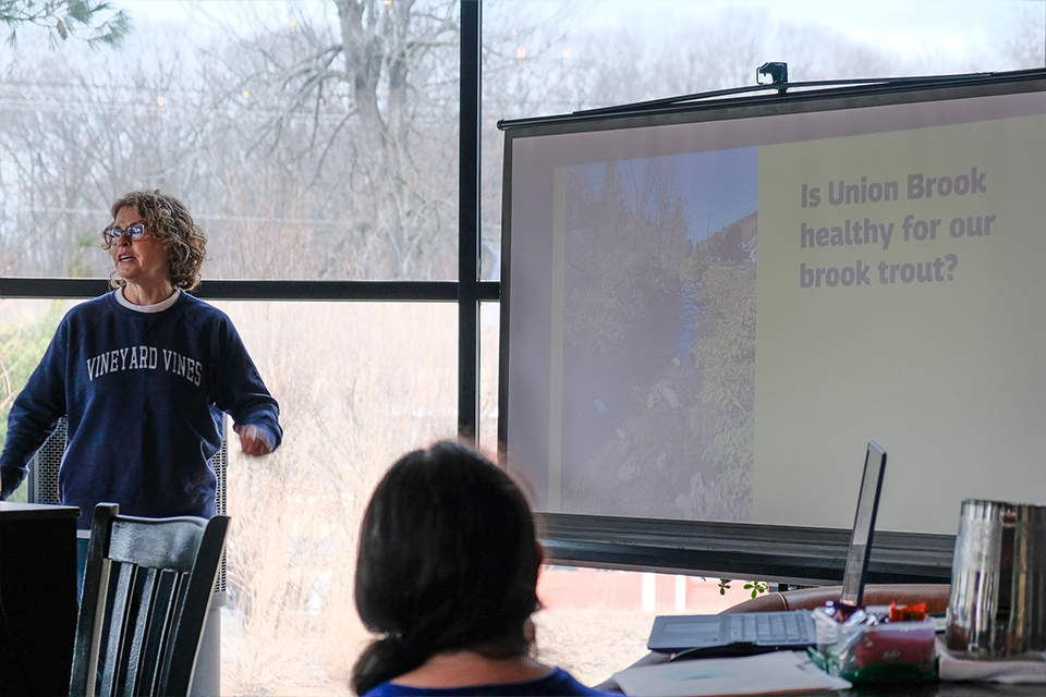 A woman stands conducts a presentation in front of a large projector screen that reads is union brook healthy for our brook trout