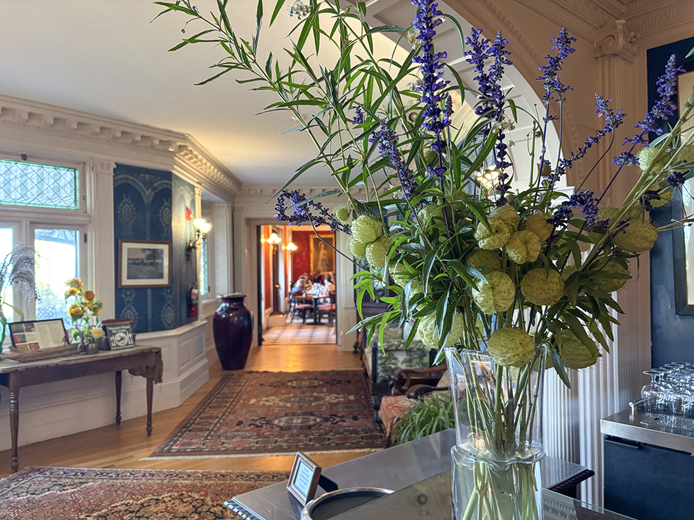 large floral arrangement on table in foreground, with long hall leading to door looking into a dining restaurant