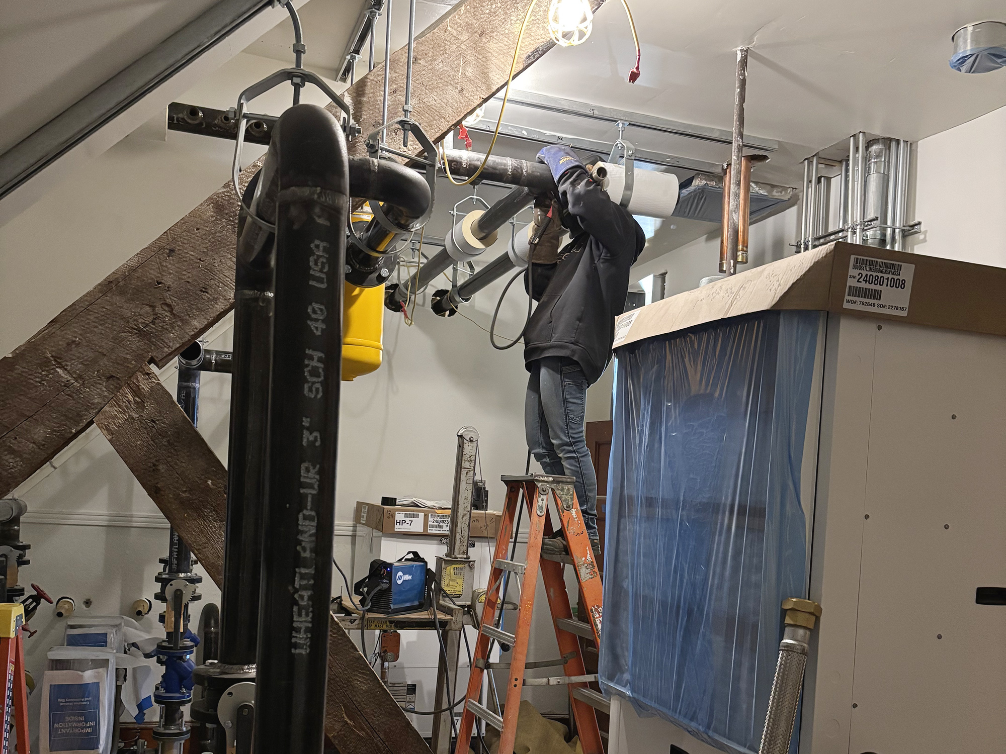 welder on a ladder welding pipes in a Coach Barn utility room 