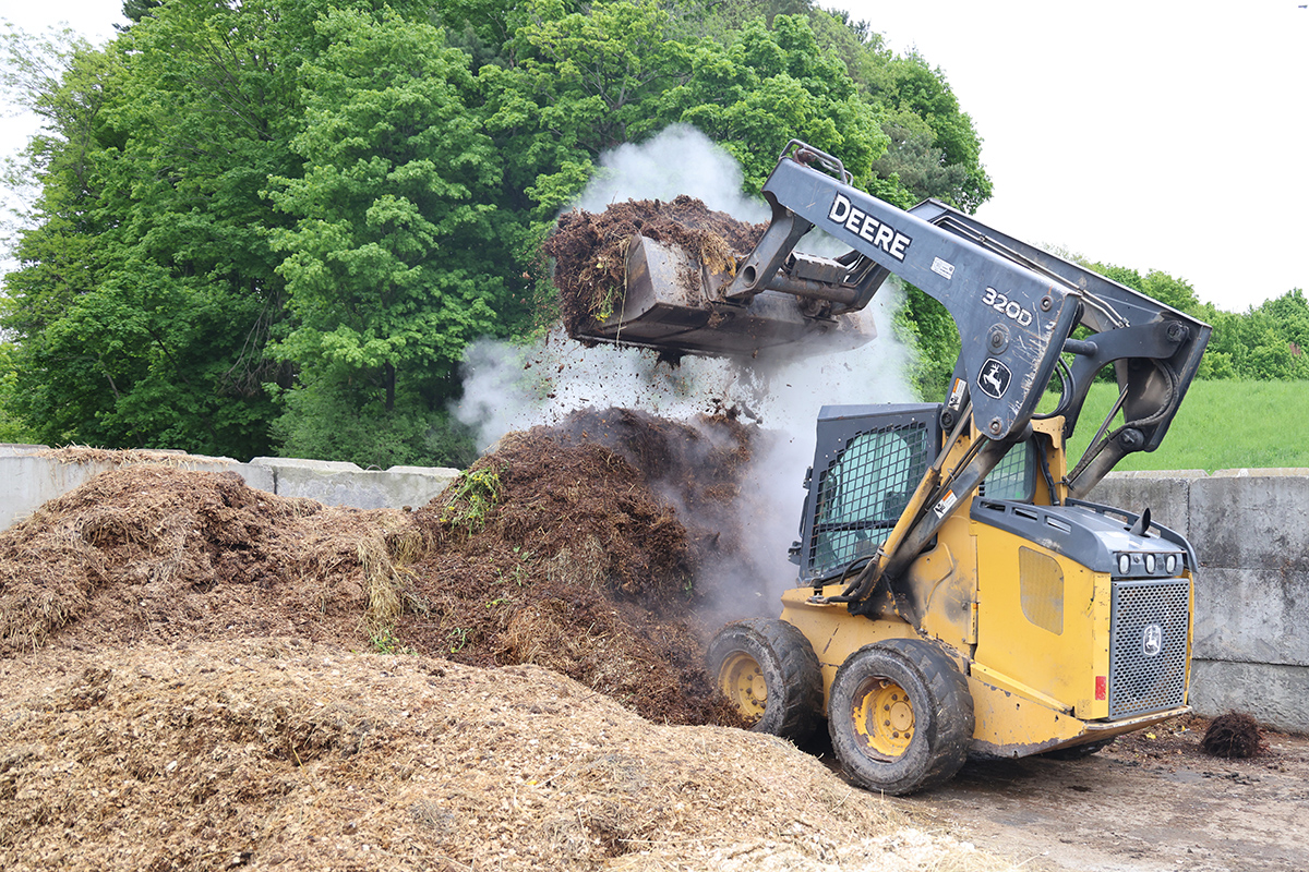 skidder turning compost in a concrete bunker area with lots of hot steam rising from the compost