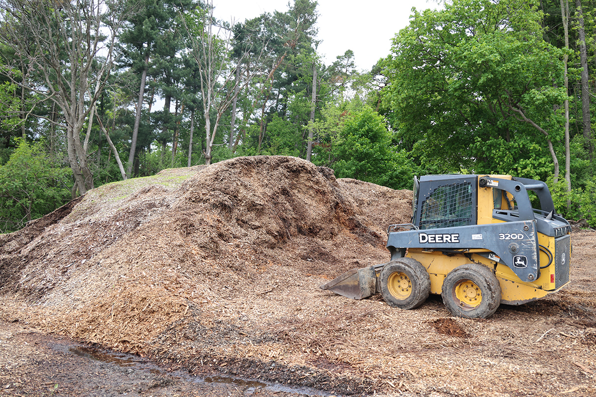 small skidder beside a large pile of wood chips