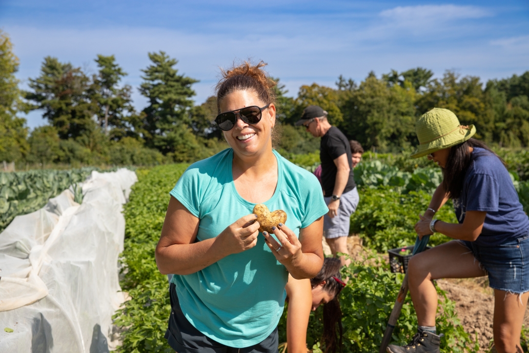 A woman smiles holding a heart shaped potato on a farm