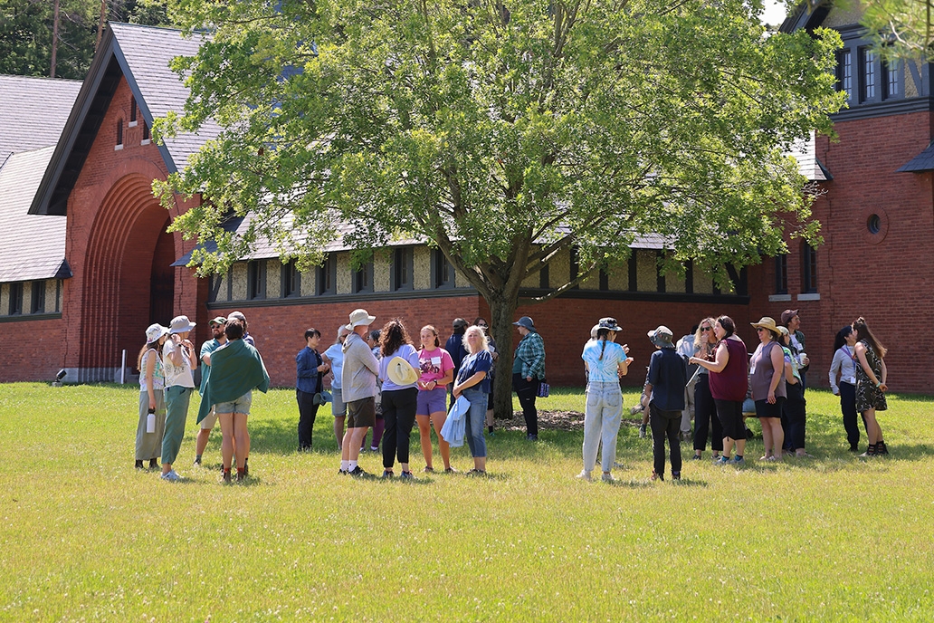 Thirty people stand in a circle outside of a large brick building