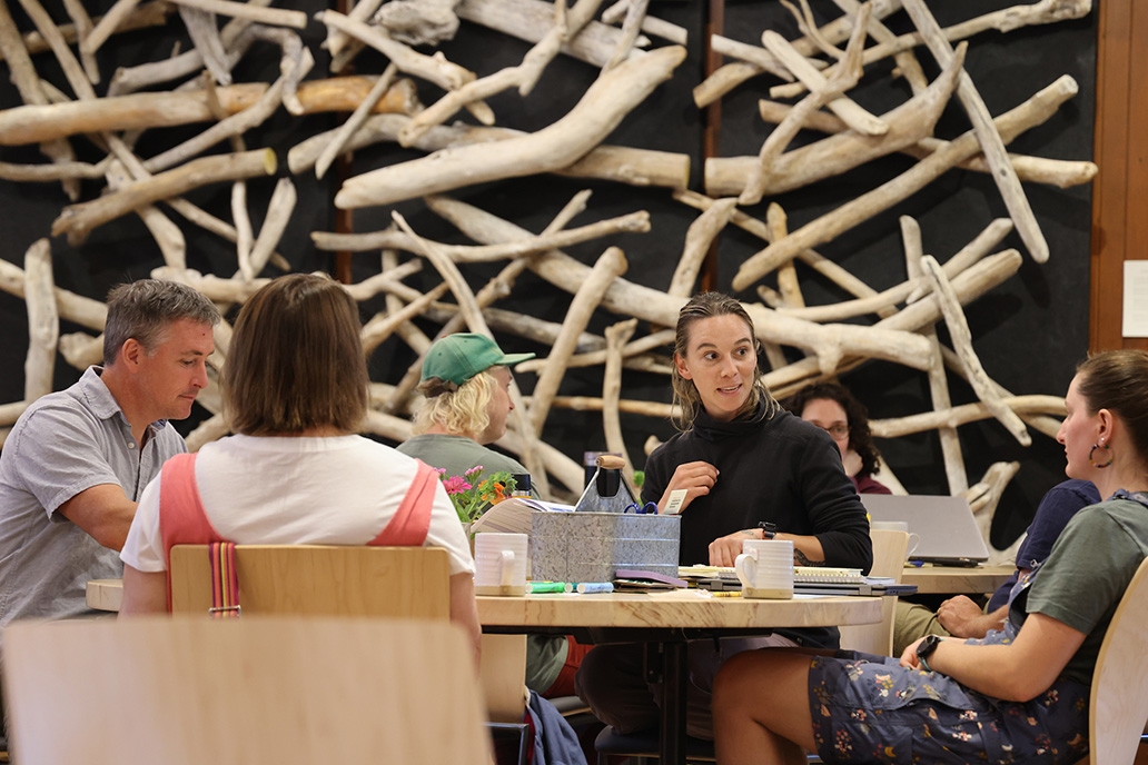 Small groups of people sit around tables in discussion in a large gathering space