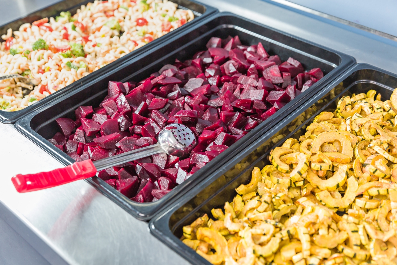Trays of colorful rice, beets, and squash on a school lunch serving line