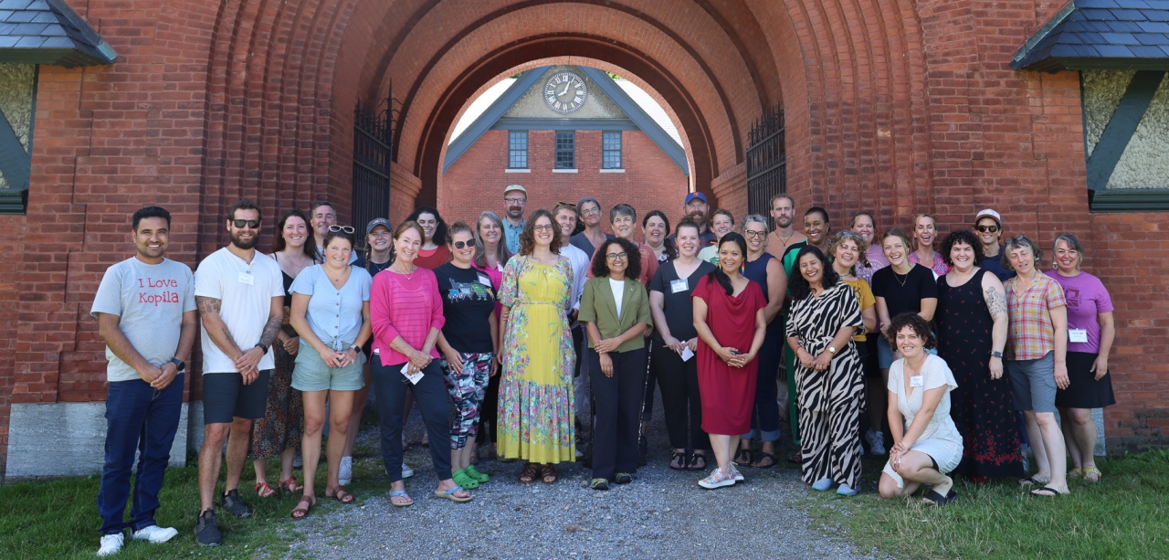 A large group of people pose and smile in front of a brick archway