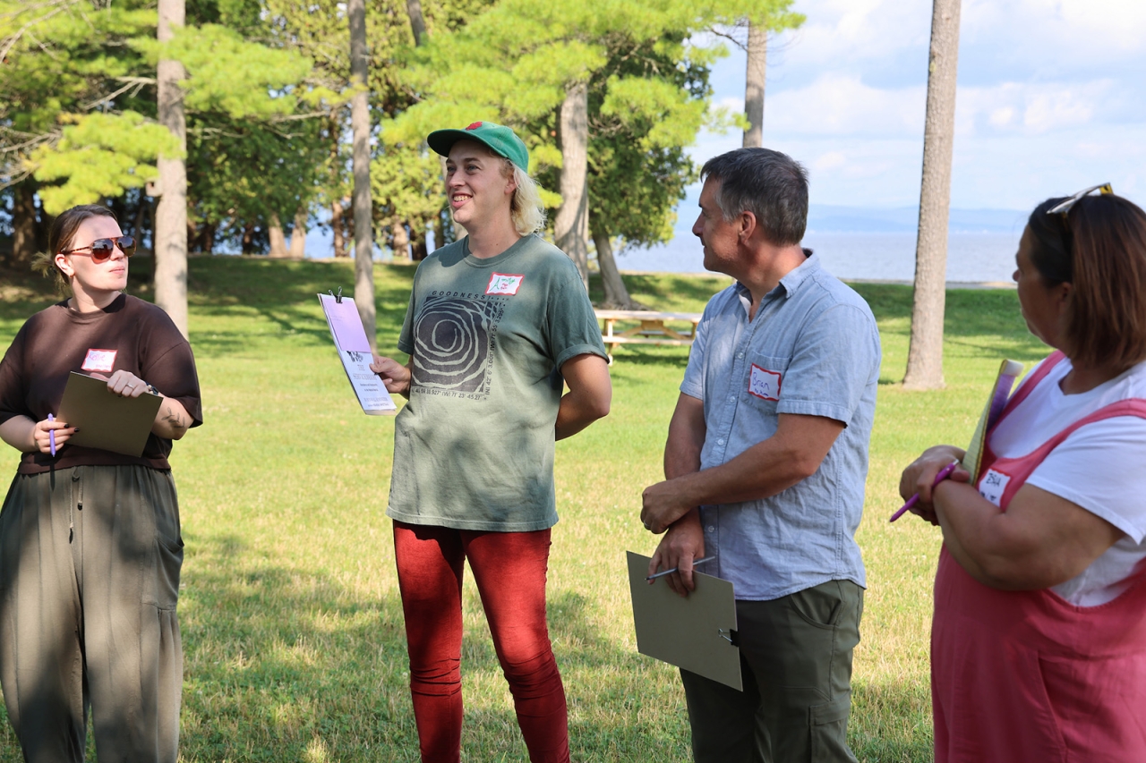 Four people stand as part of a circle smiling while in discussion outdoors