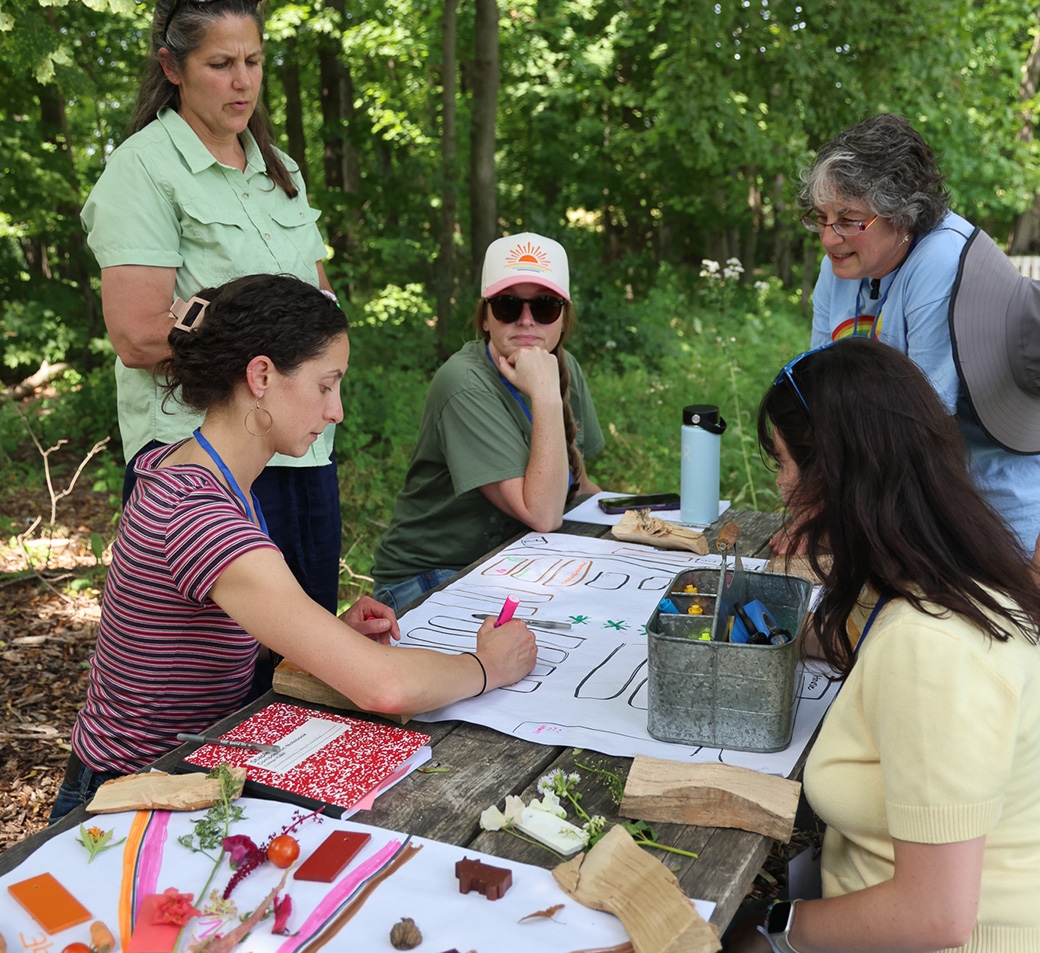 A small group of adults gather around a large piece of paper at a picnic table