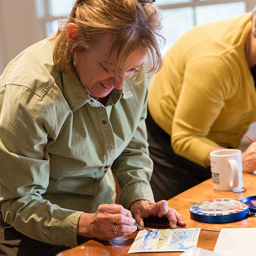 A person paints with watercolors at a table while smiling