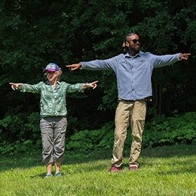 Two people stand on a green grassy lawn with arms outstretched pointing and smiling