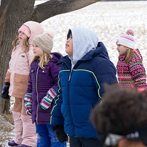 Four young children in winter clothes gaze in wonder at a tree