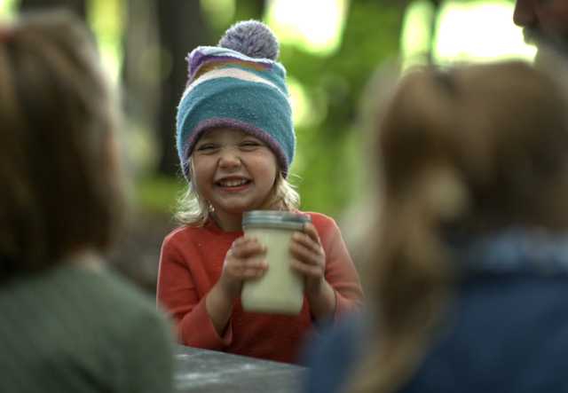 A child smiles as she shakes a jar of cream to transform it into butter.