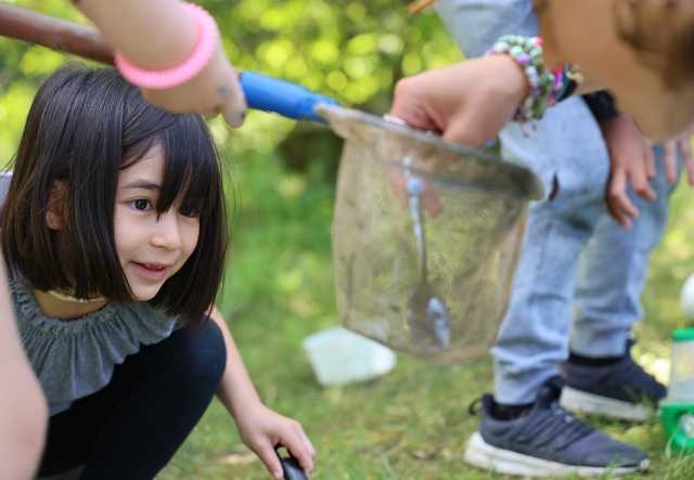A young person gazes at a small net holding discoveries from a pond and smiles
