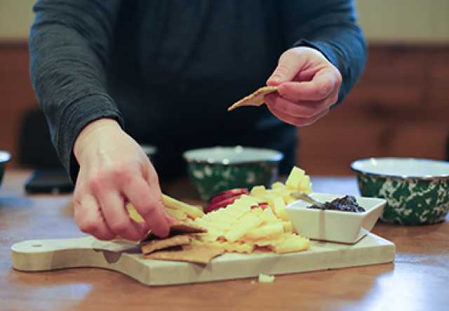 person's hands placing crackers onto a cheese board with cheddar, apple, jam